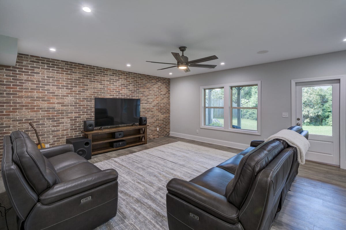 Basement media room with brick accent wall and leather recliners in Atlanta by Silver Oak Remodel