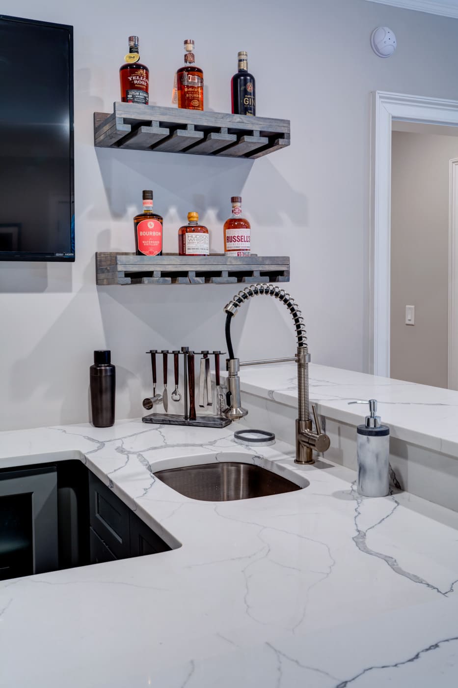 Marble-topped bar sink setup with cocktail tools and spirits in an Atlanta custom home built by Silver Oak Remodeli