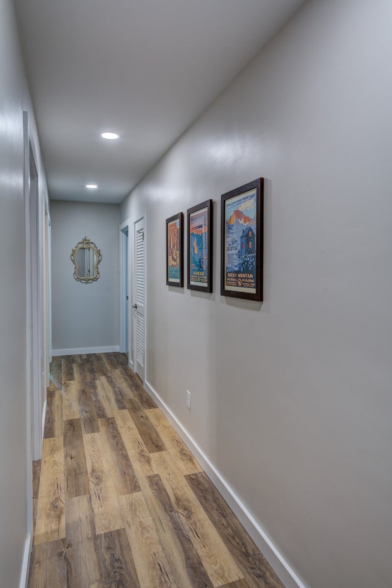 Renovated basement hallway with wood-look flooring and framed art in Atlanta GA by Silver Oak Remodel