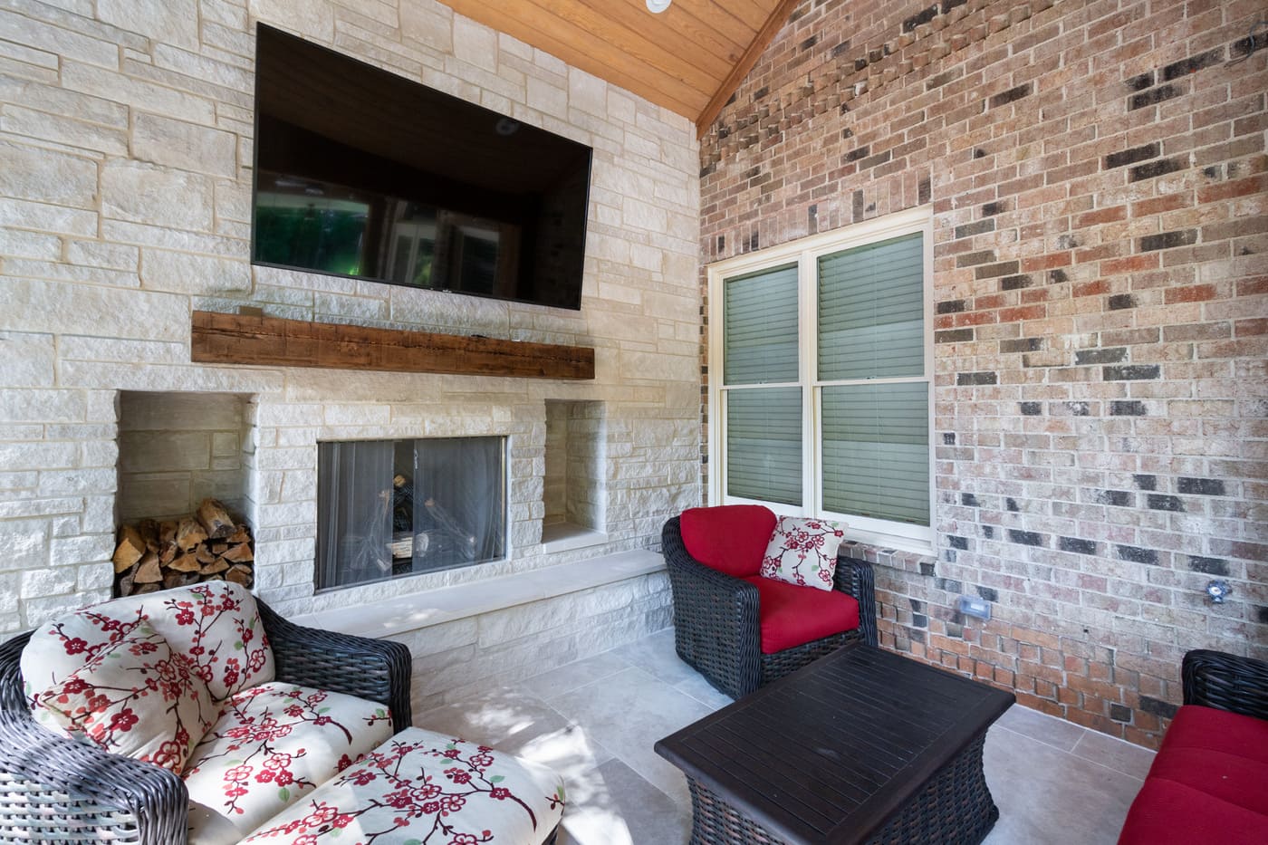 Cozy brick patio with stone fireplace and red cushioned furniture in custom home by Silver Oak Remo