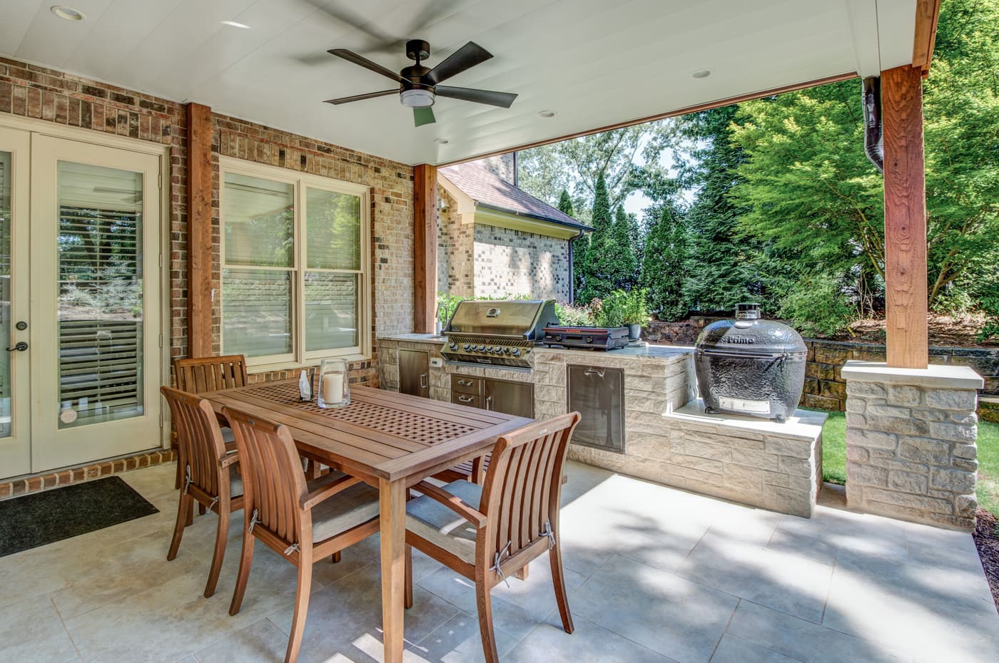 Outdoor kitchen and dining area with ceiling fan and stone counters in Atlanta custom home by Silve