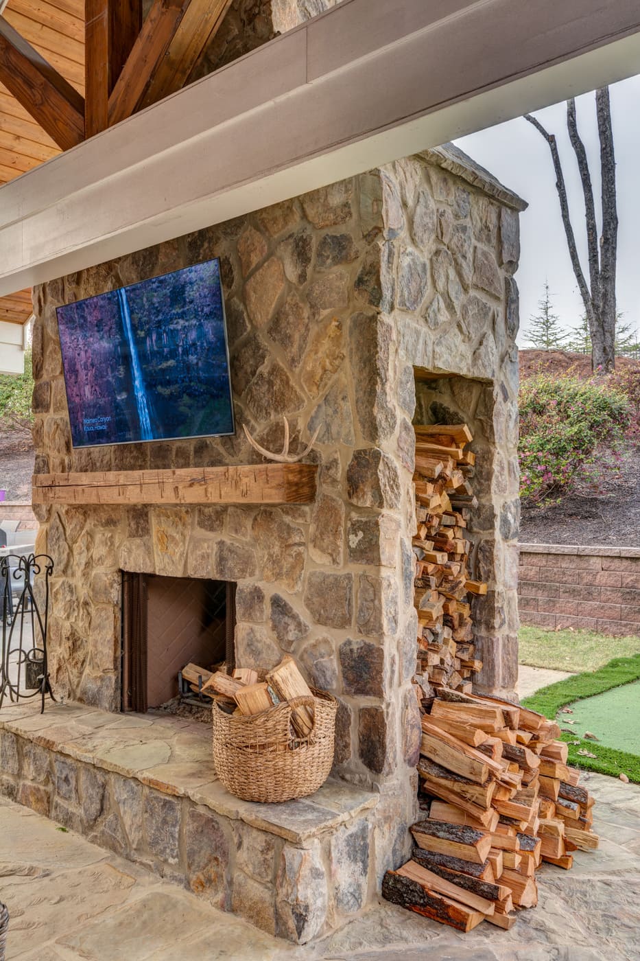 Stone fireplace with firewood storage and mounted TV under covered patio in custom Atlanta home by